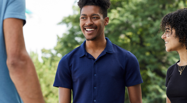 Three students smiling and talking together outdoors on a campus.